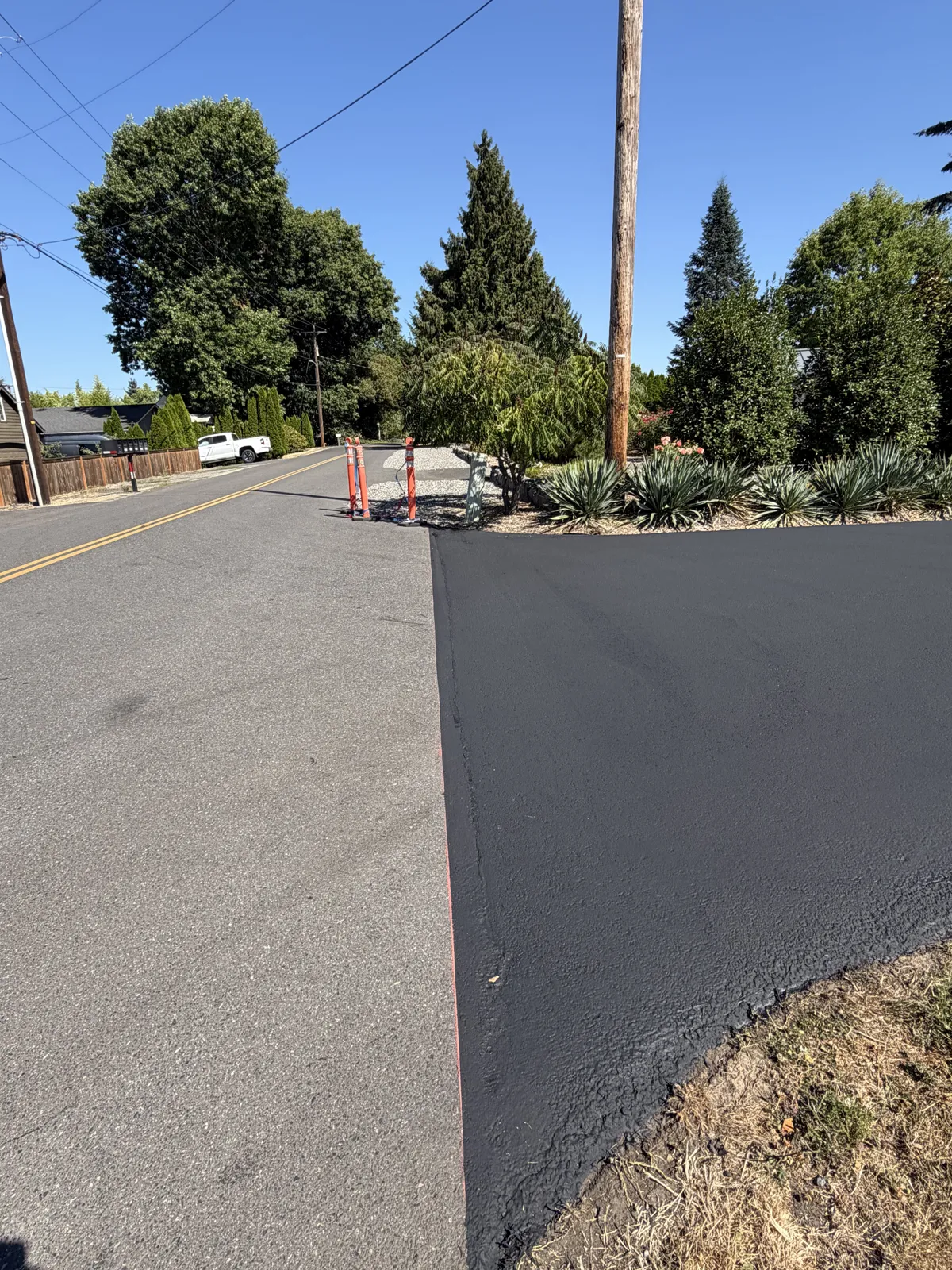 Freshly sealcoated black driveway apron next to an untreated gray asphalt road